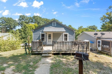 View of front of home with a deck, a metal roof, and a front yard