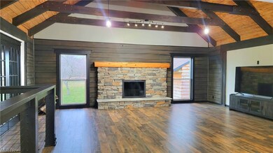 Unfurnished living room with rail lighting, a stone fireplace, dark hardwood / wood-style flooring, and lofted ceiling with beams