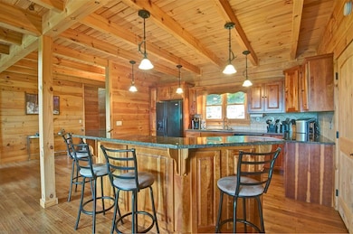 Kitchen featuring black fridge with ice dispenser, brown cabinetry, light wood finished floors, a wooden ceiling with exposed beams, and wooden walls