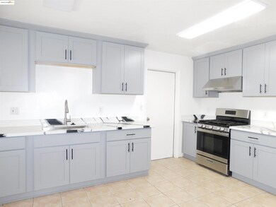 Kitchen featuring stainless steel gas range oven, gray cabinets, light countertops, under cabinet range hood, and light tile patterned floors