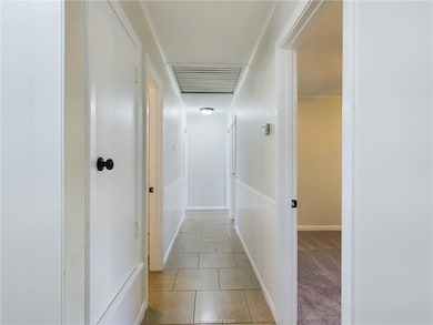 Hallway featuring light tile patterned floors, ornamental molding, and light colored carpet