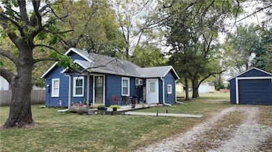 View of front of property featuring driveway, an outbuilding, roof with shingles, a detached garage, and a wall unit AC