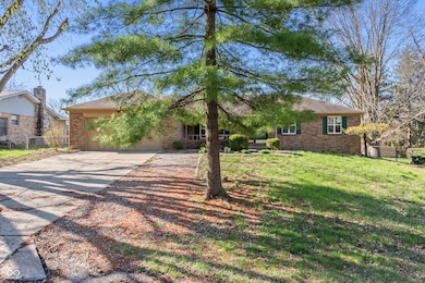 view of front of home featuring driveway, an attached garage, a front lawn, brick siding, and fence