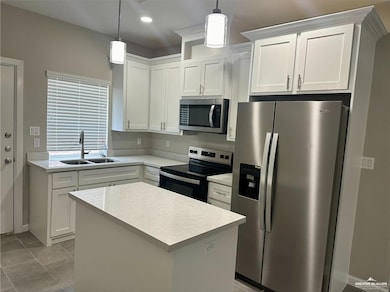 Kitchen featuring a center island, a sink, stainless steel appliances, light countertops, and white cabinetry