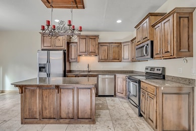 Kitchen featuring stainless steel appliances, hanging light fixtures, dark stone counters, a kitchen island, and a kitchen breakfast bar