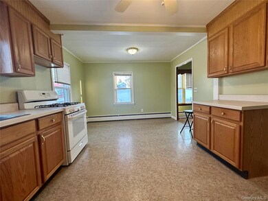 Kitchen with white range with gas stovetop, brown cabinets, light countertops, crown molding, and baseboard heating