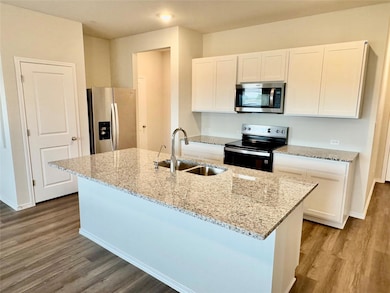 Kitchen with stainless steel appliances, white cabinetry, light stone counters, and a center island with sink