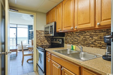 Kitchen featuring stainless steel electric range oven, brown cabinetry, decorative backsplash, light countertops, and light tile patterned floors