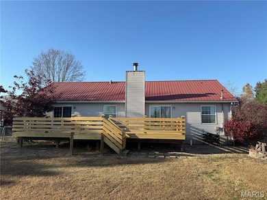 Back of house featuring a chimney, a lawn, a wooden deck, and a metal roof