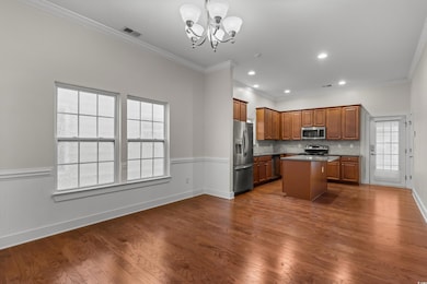 Kitchen featuring brown cabinetry, crown molding, a center island, dark wood-type flooring, and appliances with stainless steel finishes