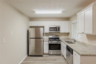 Kitchen featuring stainless steel appliances, a sink, light wood-style floors, white cabinets, and light stone counters