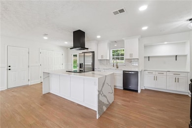 Kitchen featuring island exhaust hood, appliances with stainless steel finishes, light wood finished floors, white cabinets, and a kitchen island