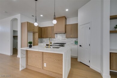 Kitchen with tasteful backsplash, light wood-type flooring, a sink, light stone counters, and visible vents