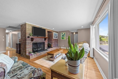 Living area with a brick fireplace, light wood-type flooring, and a textured ceiling