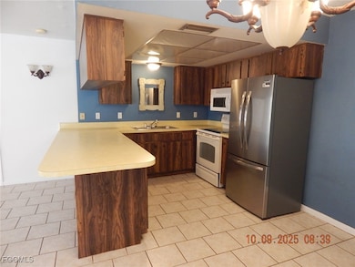 Kitchen featuring white appliances, light countertops, a peninsula, light tile patterned flooring, and brown cabinetry