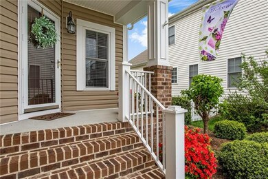 An inviting porch, surrounded by flowers and shrubs, featuring newer brick stairs and storm door.