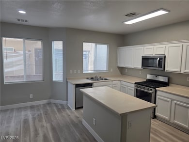 Kitchen featuring stainless steel appliances, light countertops, white cabinetry, light wood finished floors, and a textured ceiling