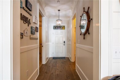 Hall with an inviting chandelier, a wainscoted wall, dark wood-type flooring, and crown molding