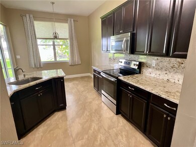 Kitchen featuring appliances with stainless steel finishes, pendant lighting, backsplash, light stone counters, and dark brown cabinetry