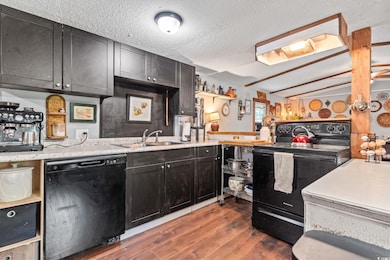 Kitchen with black appliances, wood finished floors, dark cabinets, lofted ceiling, and a textured ceiling