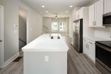 Kitchen with stainless steel appliances, a center island with sink, light stone countertops, white cabinetry, and recessed lighting