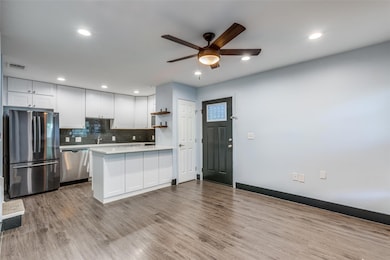 Kitchen featuring appliances with stainless steel finishes, a peninsula, light wood-style flooring, backsplash, and white cabinets