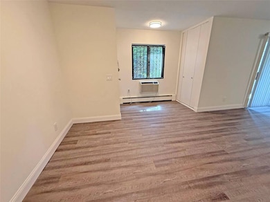 Unfurnished room with a baseboard heating unit, wood finished floors, and a wall mounted AC