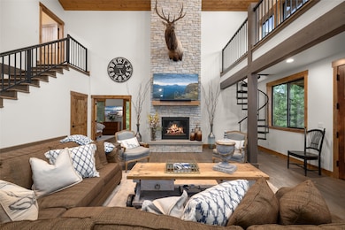 Living room with stairs, wood finished floors, a stone fireplace, a towering ceiling, and wooden ceiling