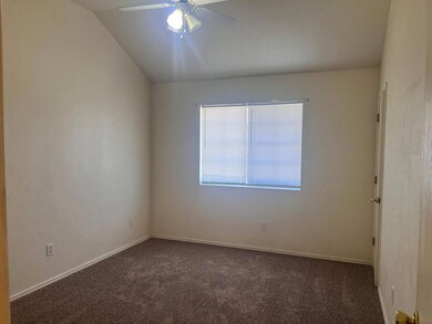 Spare room with dark carpet, a ceiling fan, vaulted ceiling, and a textured wall