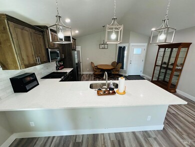 Kitchen featuring a peninsula, light stone counters, stainless steel appliances, dark wood-style floors, and vaulted ceiling