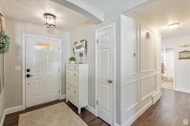 Foyer entrance with a textured ceiling, dark wood-style flooring, and arched walkways