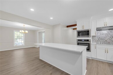 Kitchen with stainless steel appliances, light countertops, a center island, a chandelier, and white cabinets