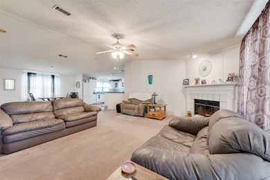 Carpeted living room featuring a textured ceiling, a tiled fireplace, and a ceiling fan