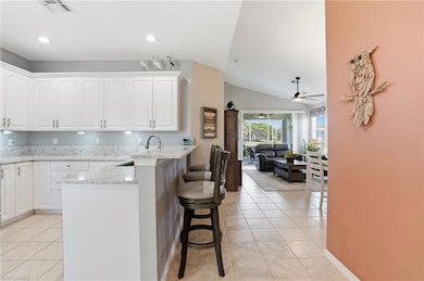 Kitchen with a breakfast bar area, light stone counters, light tile patterned floors, lofted ceiling, and white cabinetry