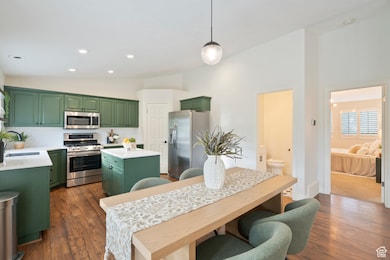 Kitchen with green cabinets, a kitchen island, appliances with stainless steel finishes, decorative backsplash, and dark wood finished floors