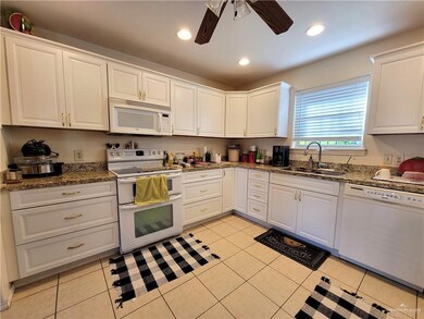 Kitchen with white appliances, light tile patterned flooring, sink, ceiling fan, and white cabinets