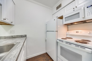 Kitchen with white appliances, white cabinetry, light countertops, dark wood-style flooring, and crown molding
