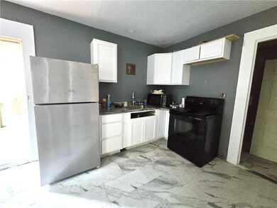 Kitchen featuring black appliances, white cabinets, light marble finish floors, and dark countertops