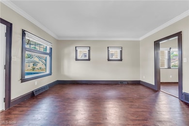Empty room with crown molding and dark wood-style floors