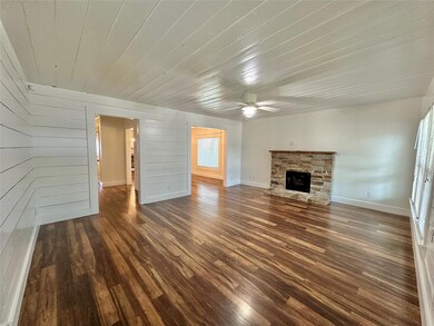 Unfurnished living room featuring a stone fireplace, ceiling fan, wood ceiling, and dark wood-type flooring
