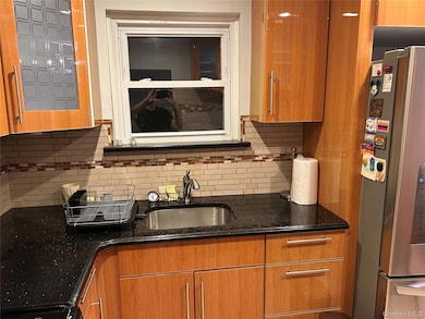 Kitchen featuring freestanding refrigerator, dark stone counters, backsplash, brown cabinetry, and glass insert cabinets
