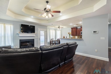 Living area featuring a raised ceiling, dark wood-style floors, a ceiling fan, recessed lighting, and a glass covered fireplace