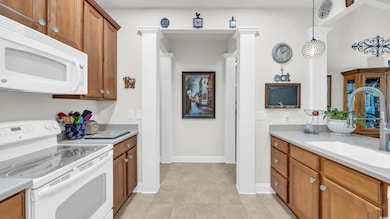 Kitchen with brown cabinetry, white appliances, light countertops, and light tile patterned floors
