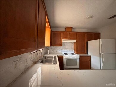 Kitchen featuring white appliances, sink, decorative backsplash, and a textured ceiling