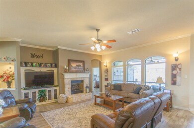 Living area with light wood-style floors, crown molding, ceiling fan, arched walkways, and a stone fireplace