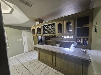 Kitchen with kitchen peninsula, dark brown cabinets, sink, refrigerator with ice dispenser, and light tile floors