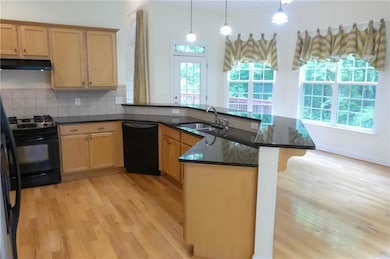 Kitchen with black appliances, under cabinet range hood, light wood finished floors, a peninsula, and a sink