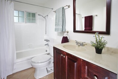 Guest bathroom with single vanity, framed dressing mirror, mirrored medicine cabinet, tiled tub/shower, high-efficiency single flush commode, privacy window and tiled floors.