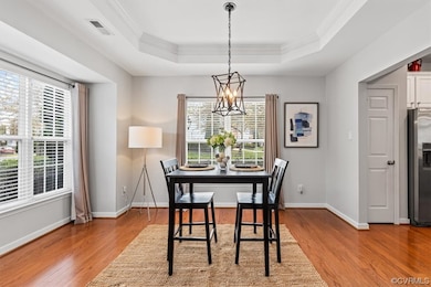 Dining space with a wealth of natural light, light hardwood floors, an inviting chandelier, and a tray ceiling