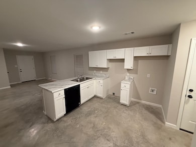 Kitchen with white cabinetry, black dishwasher, sink, and light stone counters